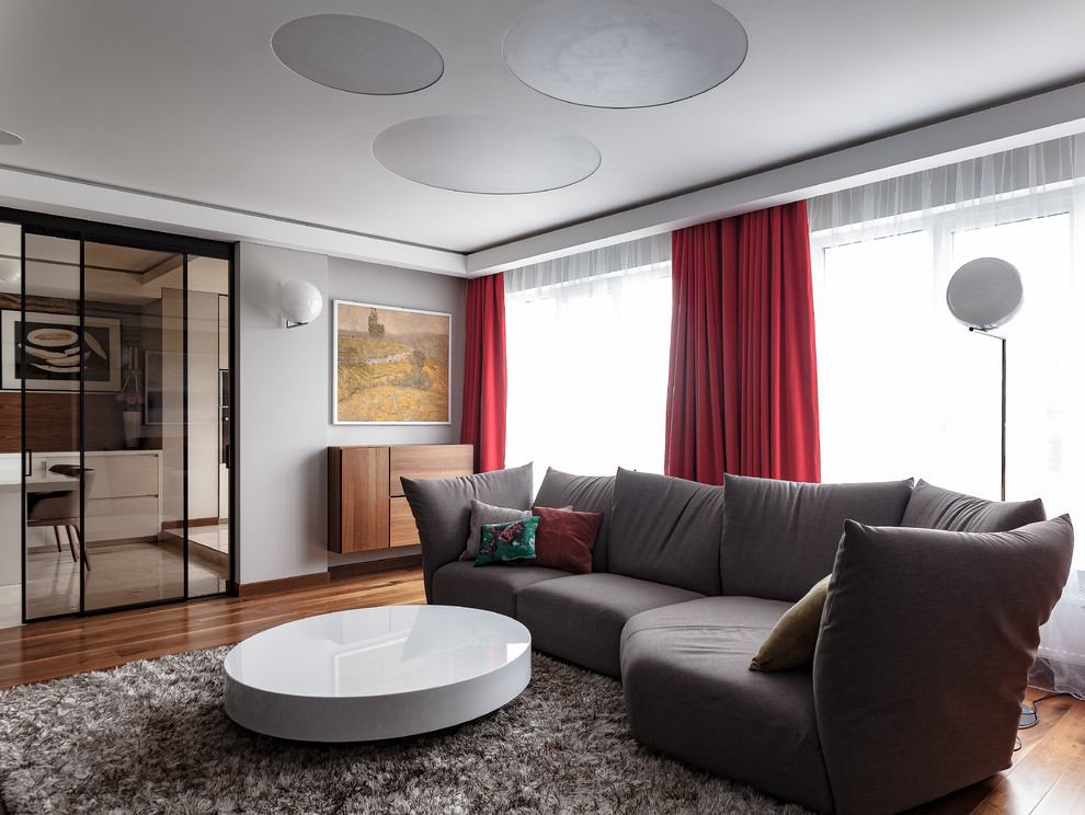 Cette image montre un salon design de taille moyenne et fermé avec un mur gris, un téléviseur dissimulé, un sol marron, une salle de réception, un sol en bois brun et éclairage.