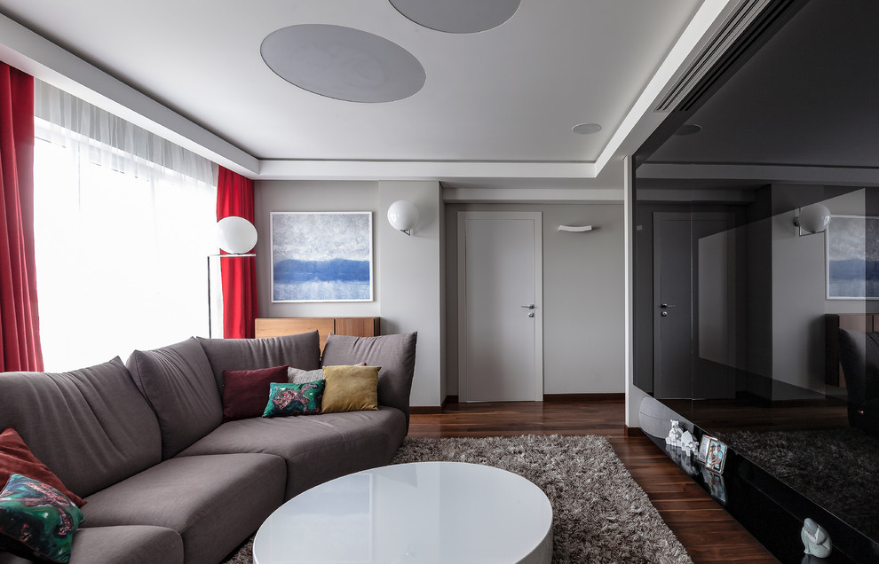 Inspiration pour un salon design de taille moyenne et fermé avec un mur gris, parquet foncé, un téléviseur dissimulé et un sol marron.