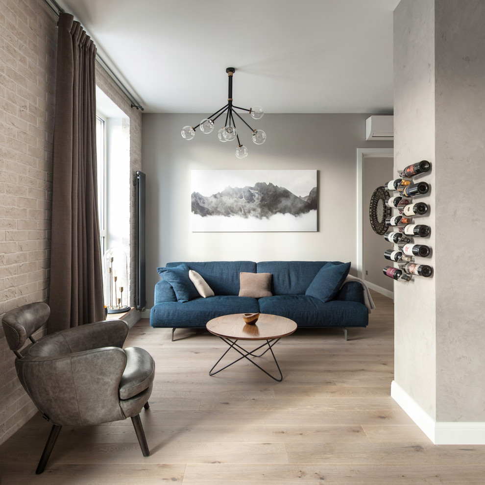 Стильный дизайн: гостиная комната в современном стиле с серыми стенами, светлым паркетным полом, бежевым полом и синим диваном - последний тренд