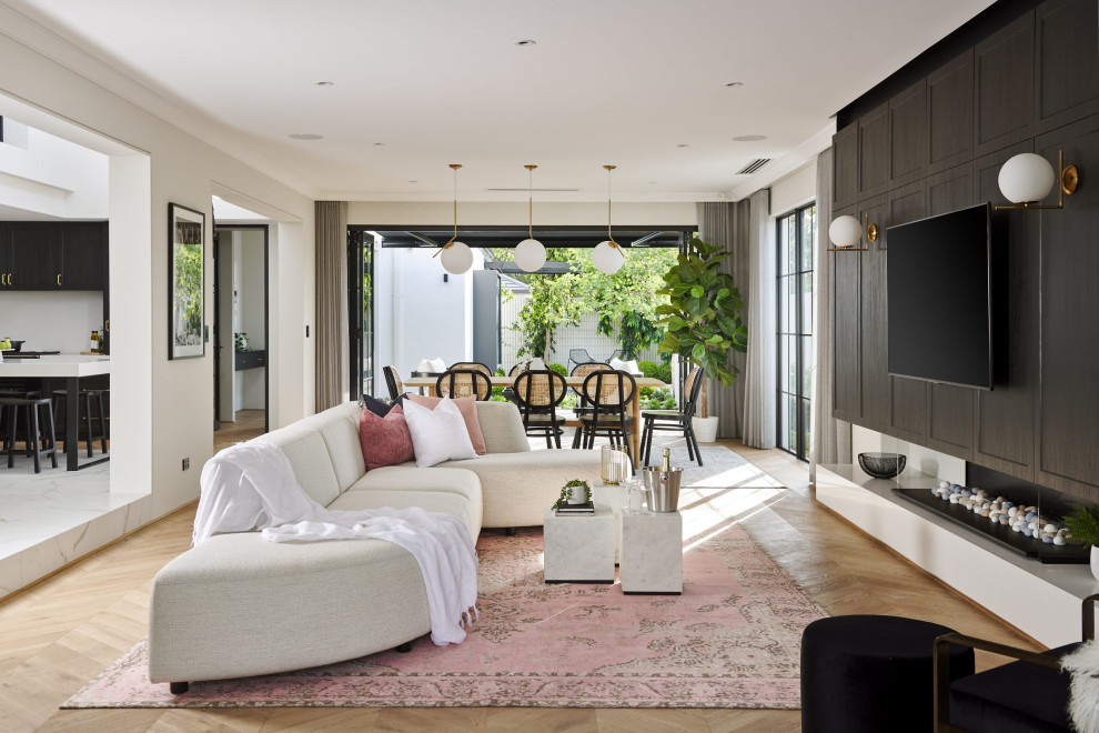На фото: открытая гостиная комната в стиле неоклассика (современная классика) с белыми стенами, светлым паркетным полом, горизонтальным камином, телевизором на стене и коричневым полом с