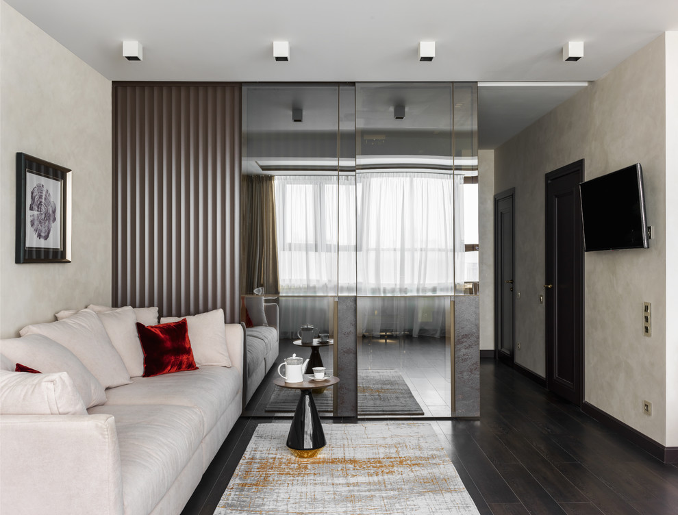 На фото: открытая гостиная комната в современном стиле с бежевыми стенами, телевизором на стене и темным паркетным полом без камина с