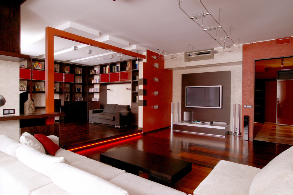 Пример оригинального дизайна: большая открытая гостиная комната в современном стиле с красными стенами, темным паркетным полом и телевизором на стене