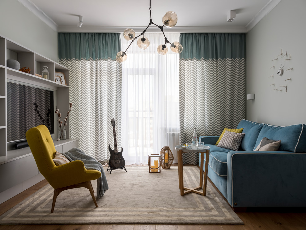 На фото: открытая гостиная комната в скандинавском стиле с серыми стенами, паркетным полом среднего тона, коричневым полом, музыкальной комнатой, мультимедийным центром и синим диваном с