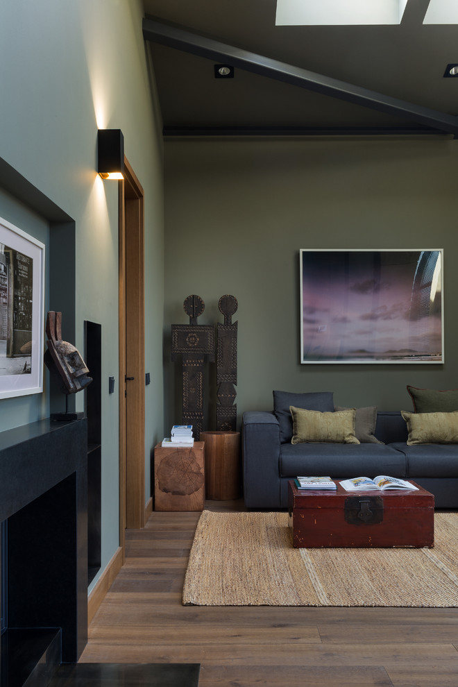 Immagine di un piccolo soggiorno contemporaneo stile loft con pareti verdi, pavimento in legno massello medio, camino classico, cornice del camino in pietra, pavimento marrone e tappeto