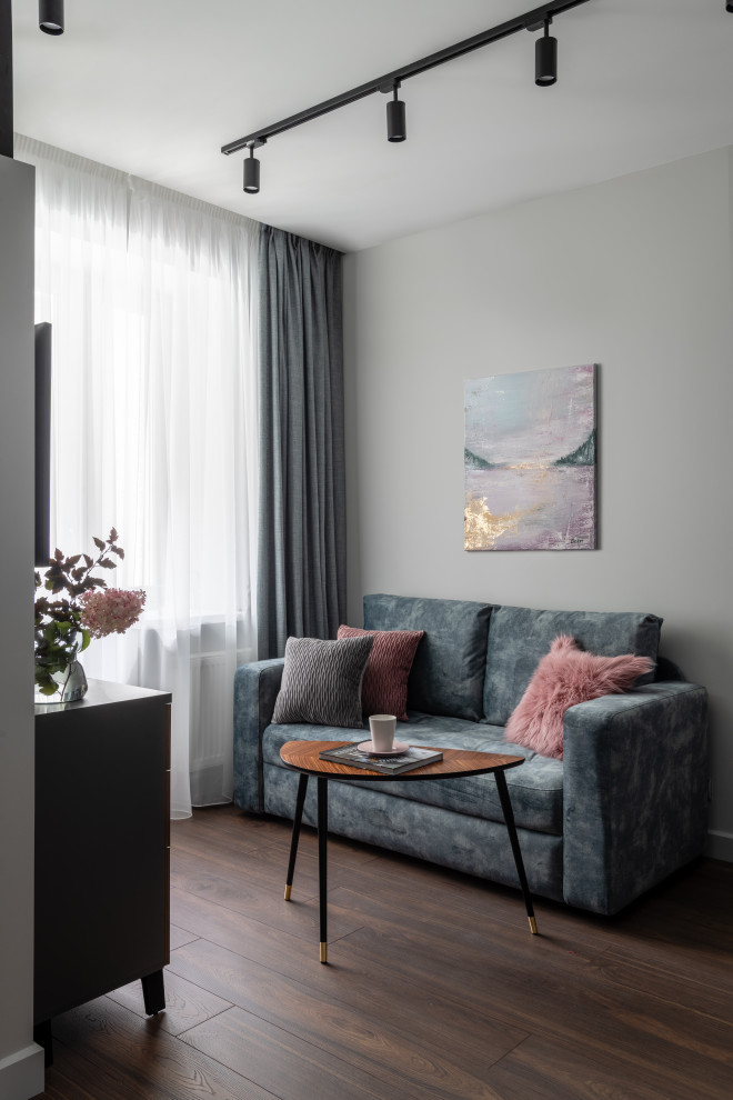 Modelo de salón abierto actual de tamaño medio con paredes grises, suelo laminado, televisor colgado en la pared y suelo marrón