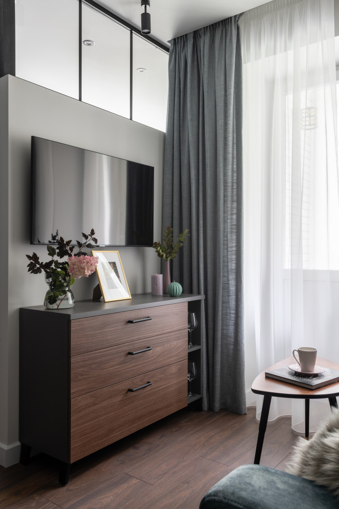 Стильный дизайн: открытая, объединенная гостиная комната среднего размера в современном стиле с серыми стенами, полом из ламината, телевизором на стене и коричневым полом - последний тренд