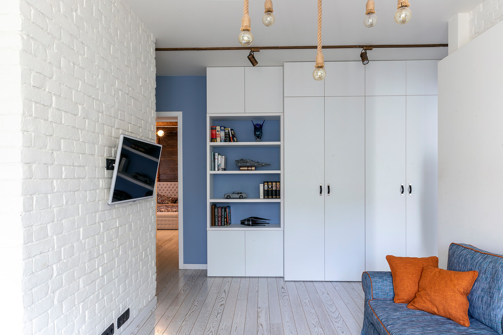 This is an example of a medium sized scandinavian open plan living room in Moscow with white walls, light hardwood flooring, a wall mounted tv and white floors.