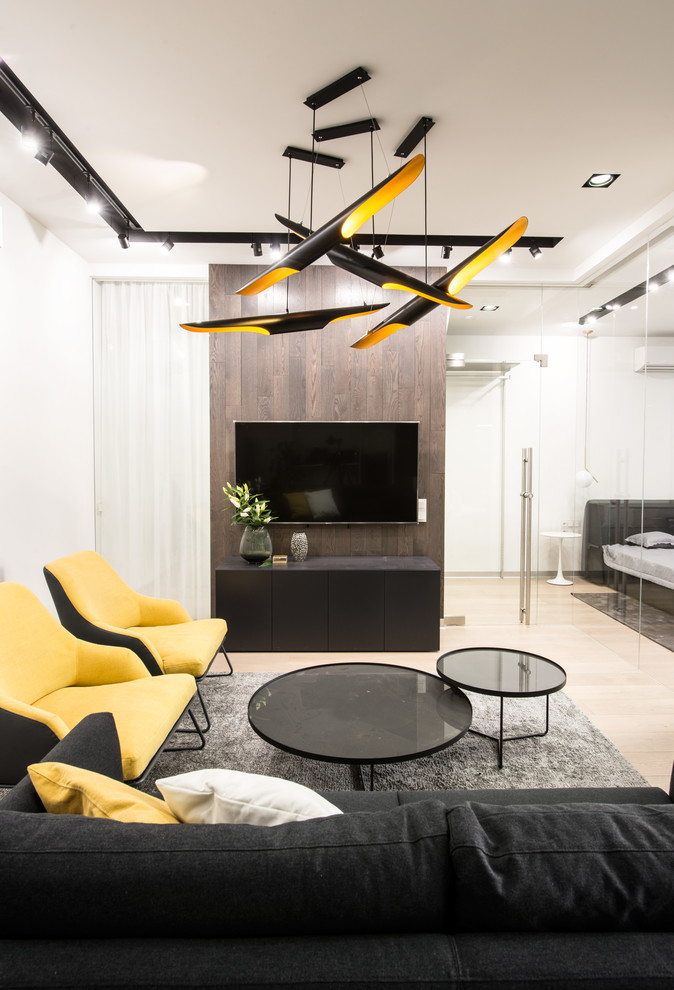 Idée de décoration pour un salon design avec un mur blanc, parquet clair, un téléviseur fixé au mur, un sol beige et canapé noir.