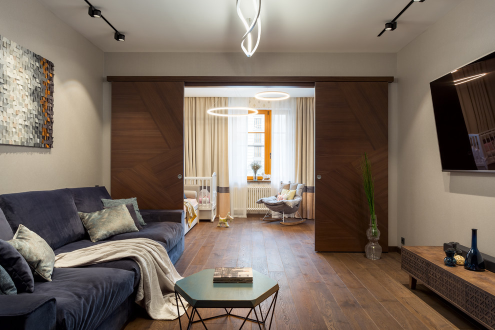 Inspiration pour une grande salle de séjour design avec un mur beige, un sol en bois brun, un téléviseur fixé au mur, un sol marron et éclairage.