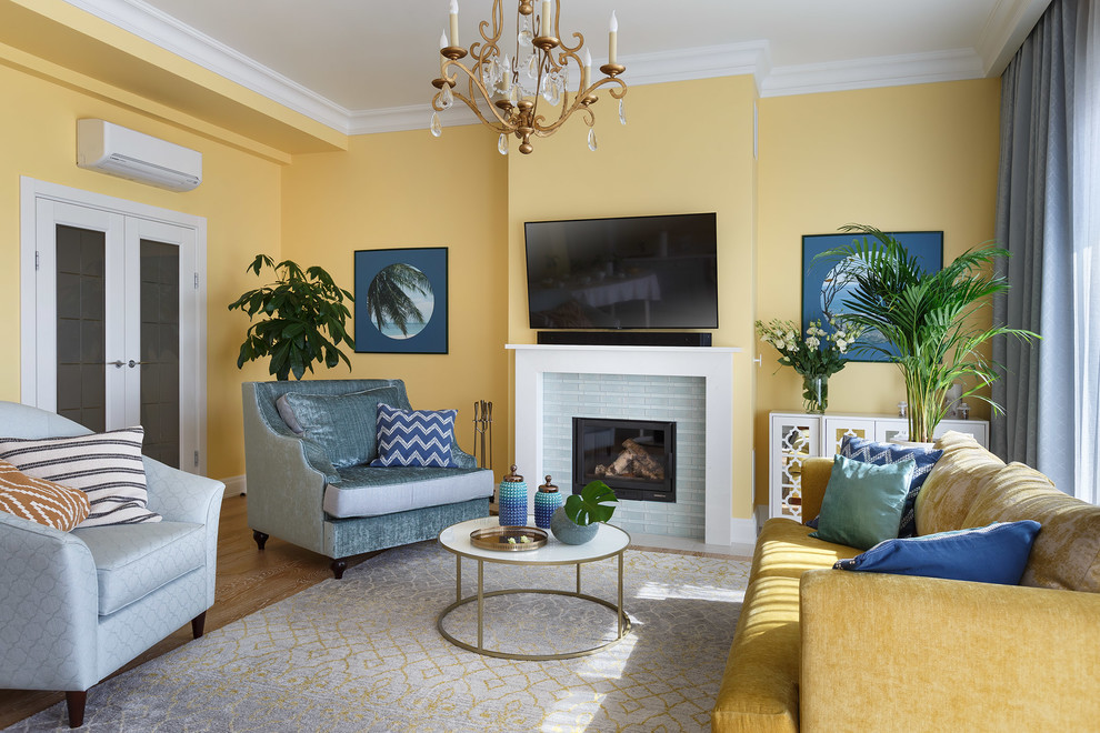 Свежая идея для дизайна: большая парадная, объединенная гостиная комната в стиле неоклассика (современная классика) с желтыми стенами, паркетным полом среднего тона, стандартным камином, телевизором на стене, коричневым полом и фасадом камина из плитки - отличное фото интерьера