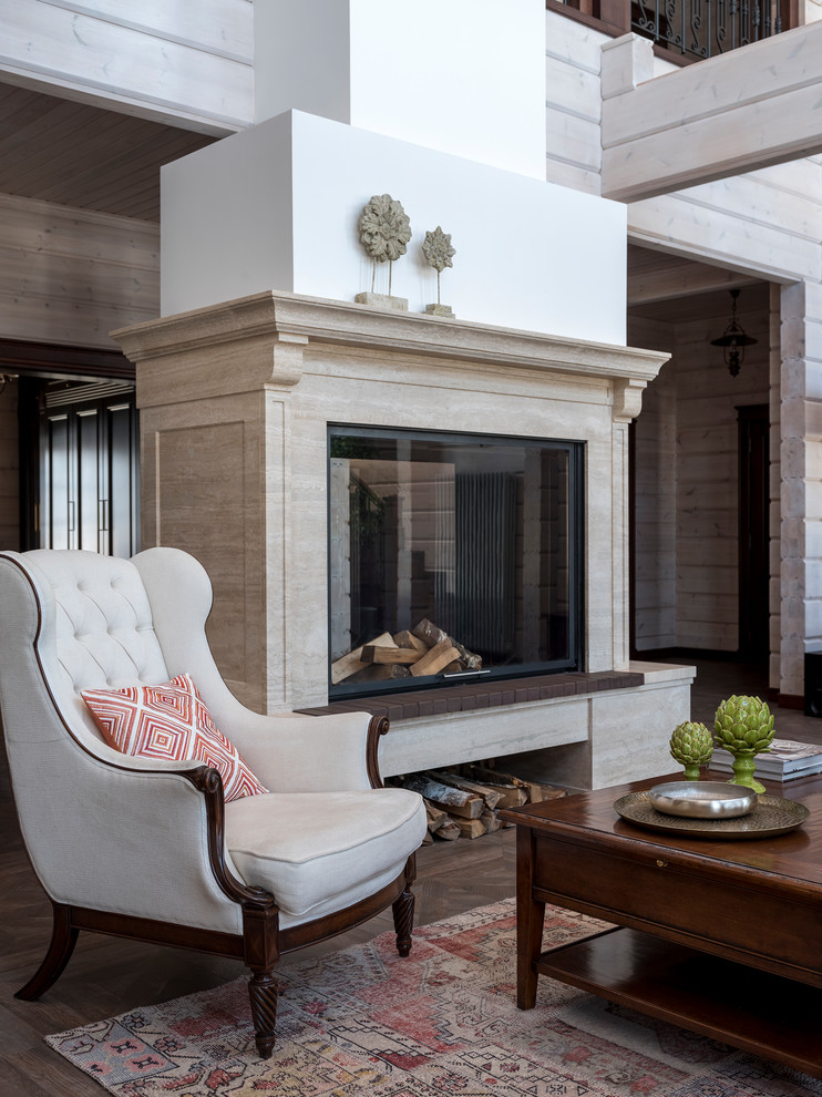 Стильный дизайн: гостиная комната в стиле неоклассика (современная классика) с двусторонним камином, фасадом камина из камня и коричневым полом - последний тренд