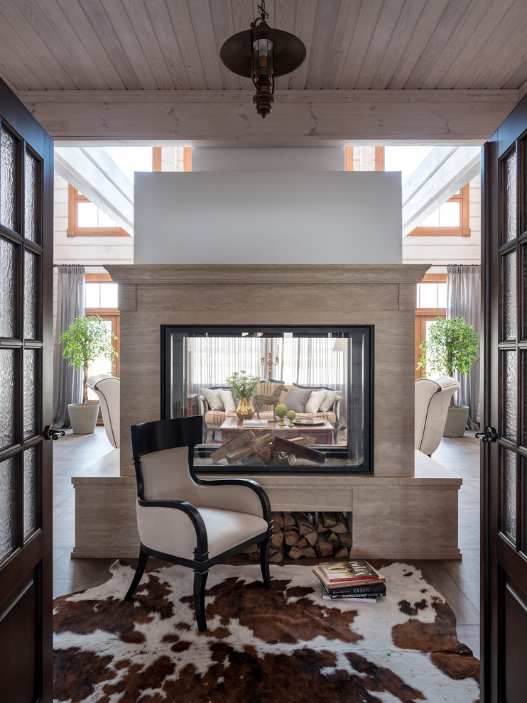 Свежая идея для дизайна: гостиная комната в стиле кантри с двусторонним камином, фасадом камина из камня и коричневым полом - отличное фото интерьера