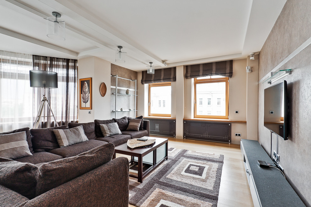 Идея дизайна: гостиная комната в современном стиле с бежевыми стенами, светлым паркетным полом, телевизором на стене и коричневым диваном