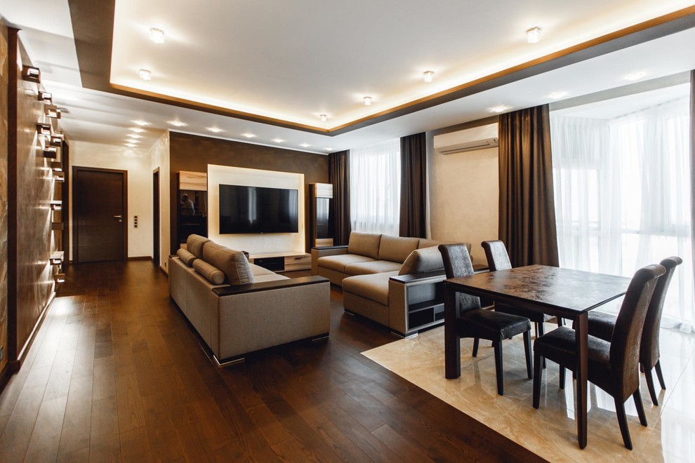 Пример оригинального дизайна: большая открытая гостиная комната в современном стиле с коричневыми стенами, темным паркетным полом, телевизором на стене и коричневым полом