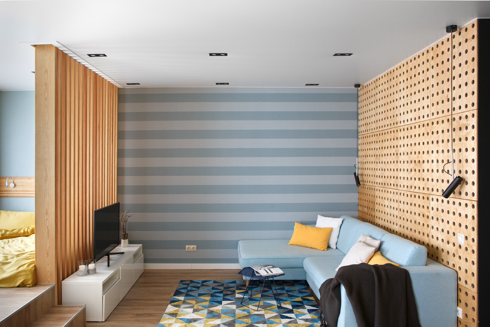 Пример оригинального дизайна: гостиная комната в современном стиле с синими стенами, паркетным полом среднего тона, телевизором на стене и коричневым полом без камина