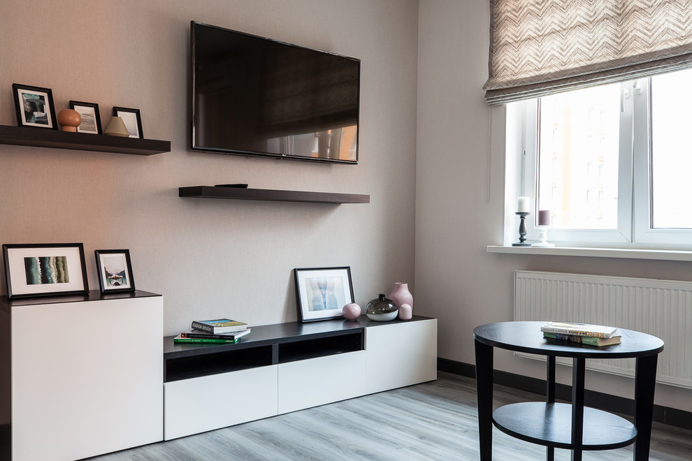 Ejemplo de salón cerrado actual de tamaño medio con paredes beige, suelo laminado, televisor colgado en la pared y suelo gris