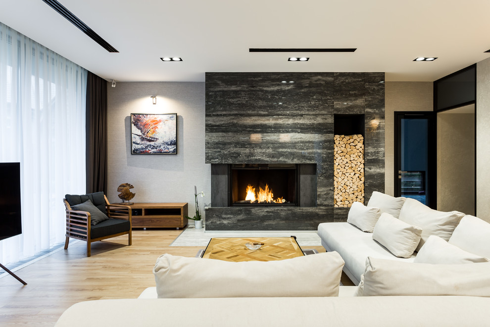 Cette image montre un grand salon design ouvert avec un mur gris, un sol en bois brun, une cheminée ribbon, un manteau de cheminée en pierre, un téléviseur indépendant et un sol beige.