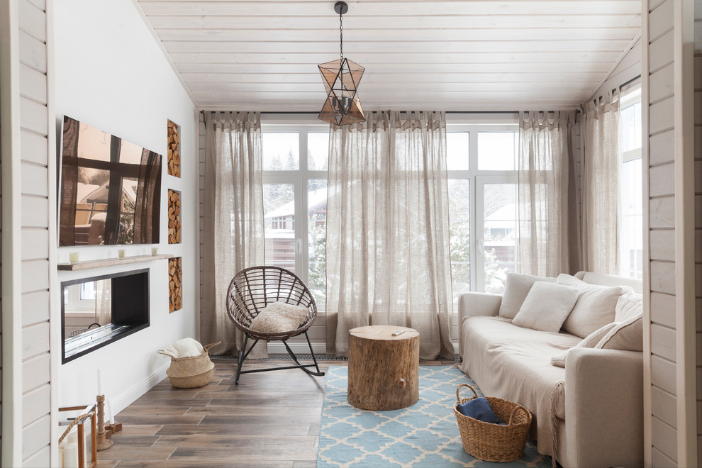 Immagine di un soggiorno nordico chiuso con pareti bianche, pavimento in legno massello medio, camino bifacciale, TV a parete e pavimento marrone