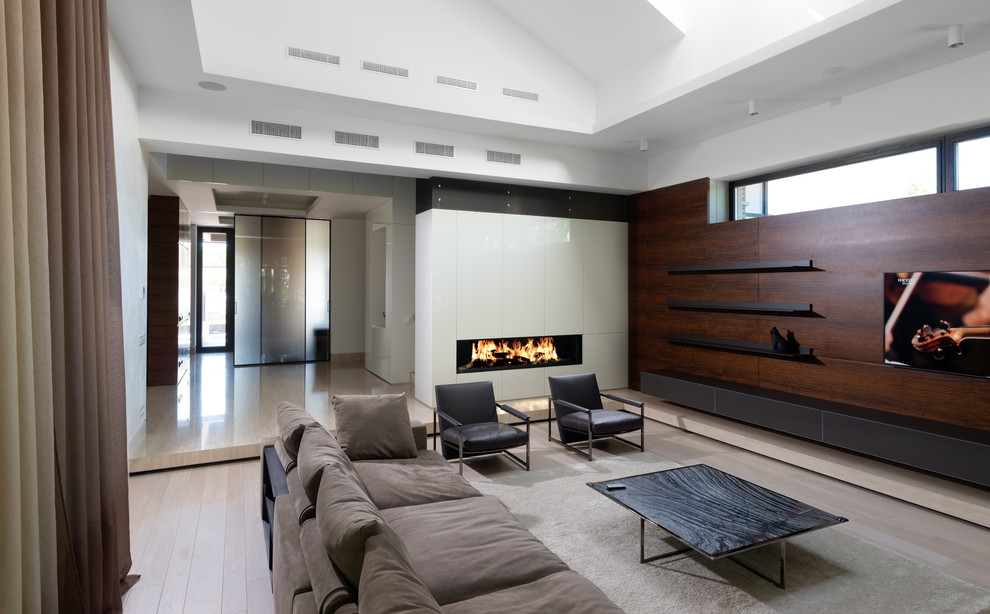 Modelo de salón contemporáneo con paredes blancas, suelo de madera clara, chimenea lineal y televisor colgado en la pared