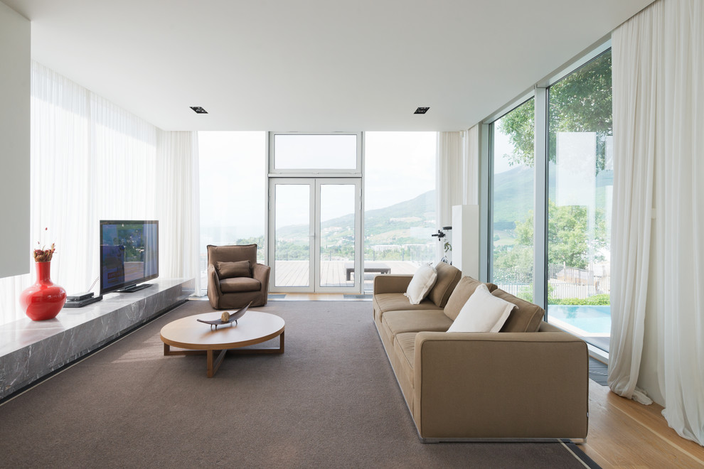 На фото: большая изолированная гостиная комната в современном стиле с отдельно стоящим телевизором, ковровым покрытием и коричневым диваном