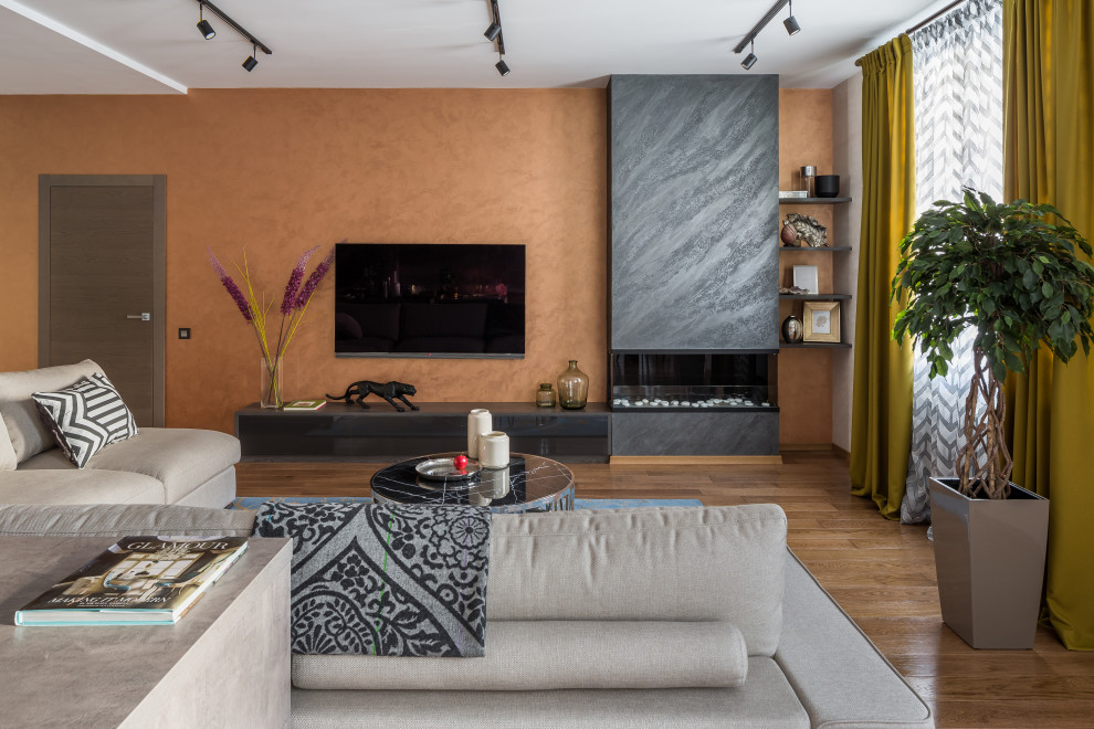 他の地域にあるコンテンポラリースタイルのおしゃれなLDK (オレンジの壁、無垢フローリング、横長型暖炉、壁掛け型テレビ、茶色い床) の写真