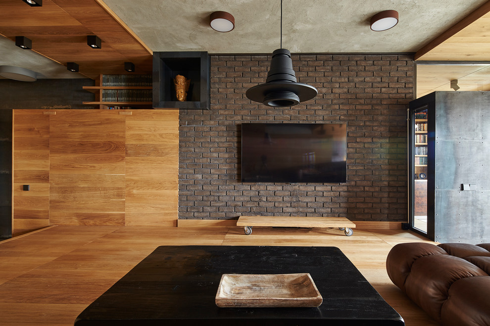 Modelo de biblioteca en casa abierta contemporánea de tamaño medio con paredes marrones, televisor colgado en la pared y suelo de madera en tonos medios