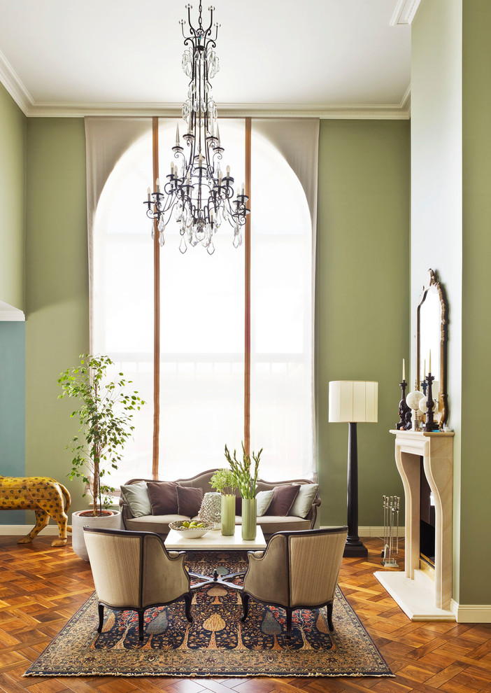 На фото: парадная, открытая гостиная комната в классическом стиле с паркетным полом среднего тона, фасадом камина из камня, зелеными стенами, стандартным камином и ковром на полу