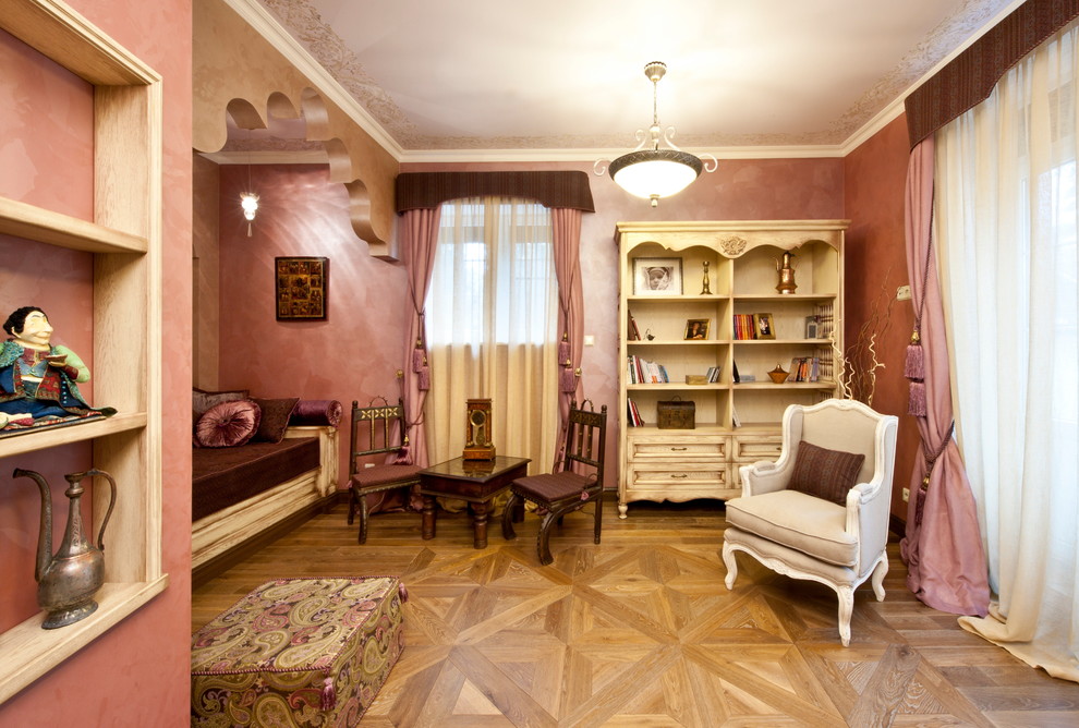 На фото: изолированная гостиная комната среднего размера в средиземноморском стиле с паркетным полом среднего тона, розовыми стенами и с книжными шкафами и полками