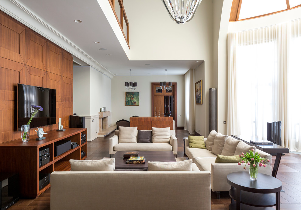 Пример оригинального дизайна: гостиная комната в современном стиле с белыми стенами, темным паркетным полом, телевизором на стене и коричневым полом