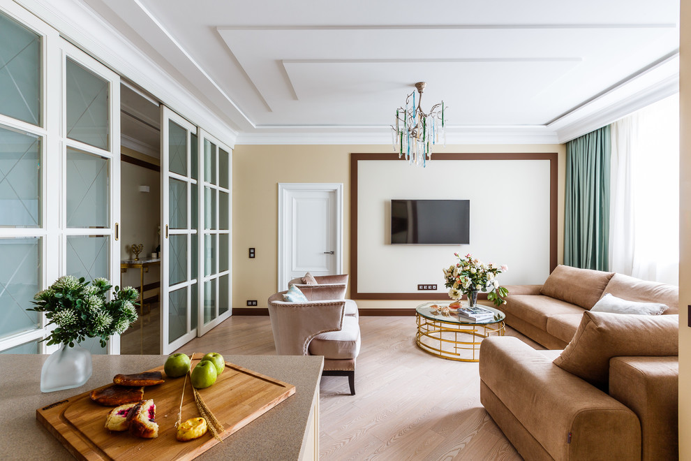 Modelo de salón para visitas abierto tradicional renovado sin chimenea con paredes beige, suelo de madera clara, televisor colgado en la pared y suelo beige