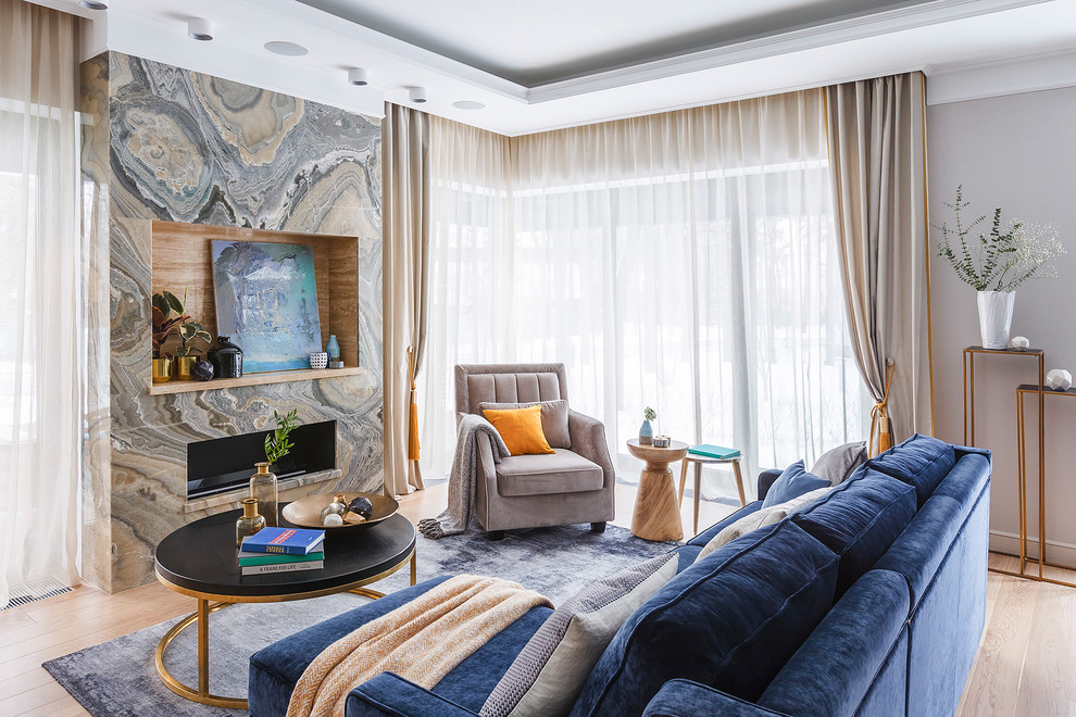 モスクワにあるトランジショナルスタイルのおしゃれなリビング (グレーの壁、淡色無垢フローリング、横長型暖炉、石材の暖炉まわり、テレビなし、ベージュの床、青いソファ) の写真