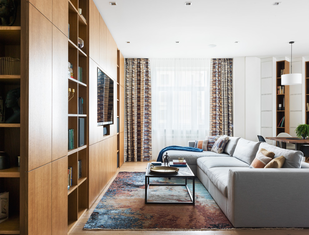 Diseño de biblioteca en casa abierta contemporánea con paredes blancas, suelo de madera clara, televisor colgado en la pared y suelo marrón