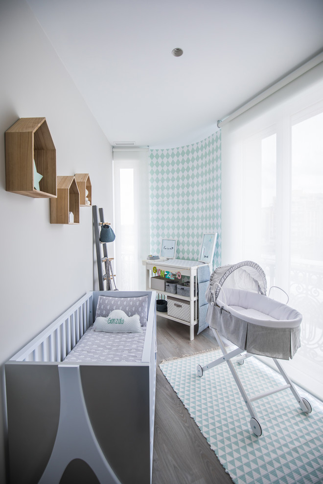 Imagen de habitación de bebé neutra actual pequeña con suelo de madera clara, paredes blancas y suelo gris
