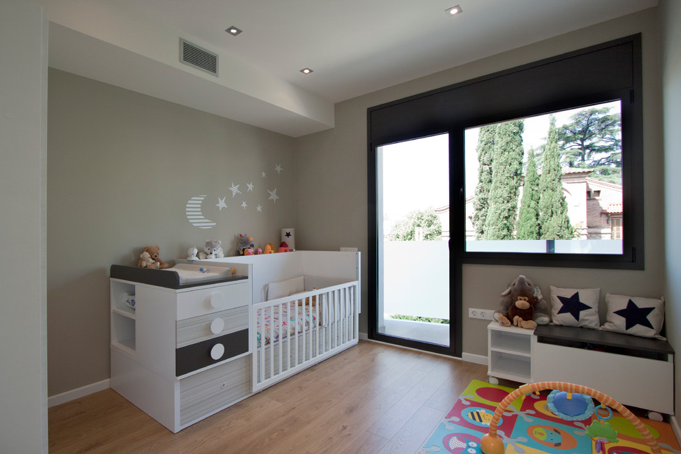 Ejemplo de habitación de bebé neutra contemporánea de tamaño medio con paredes beige y suelo de madera en tonos medios
