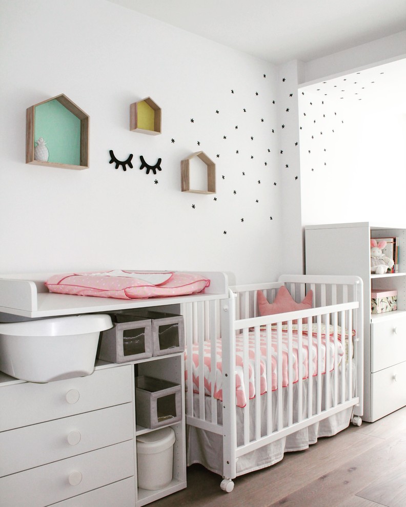 Mittelgroßes Skandinavisches Babyzimmer mit weißer Wandfarbe, braunem Holzboden und braunem Boden in Sonstige