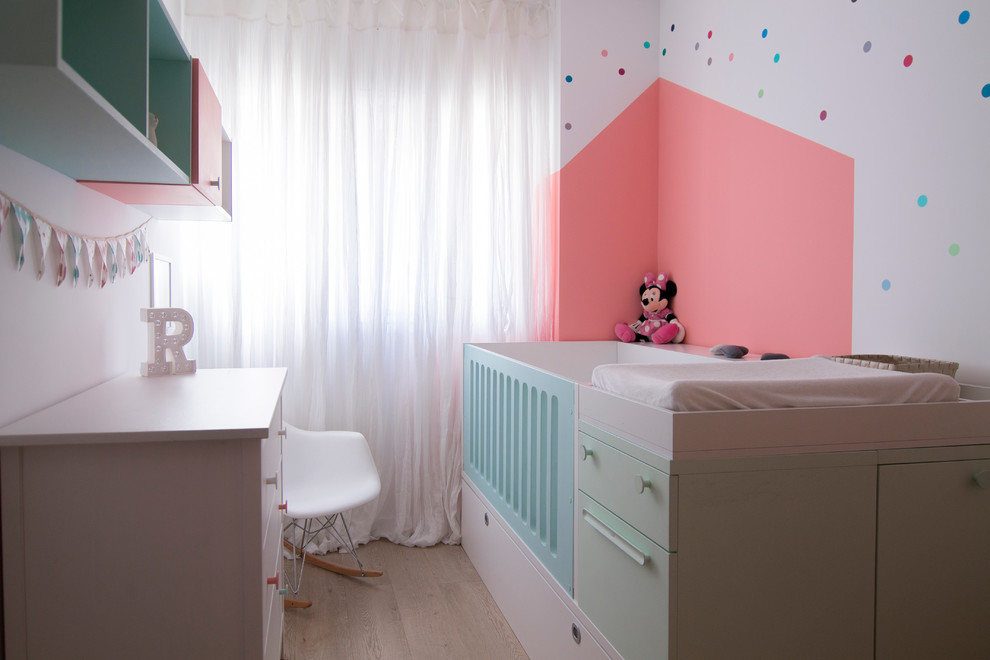 This is an example of a medium sized contemporary nursery for girls in Other with multi-coloured walls, medium hardwood flooring and beige floors.