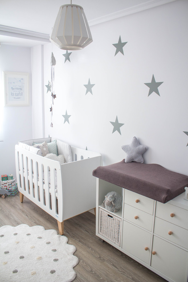 Idée de décoration pour une petite chambre de bébé neutre nordique avec un mur blanc et un sol en bois brun.