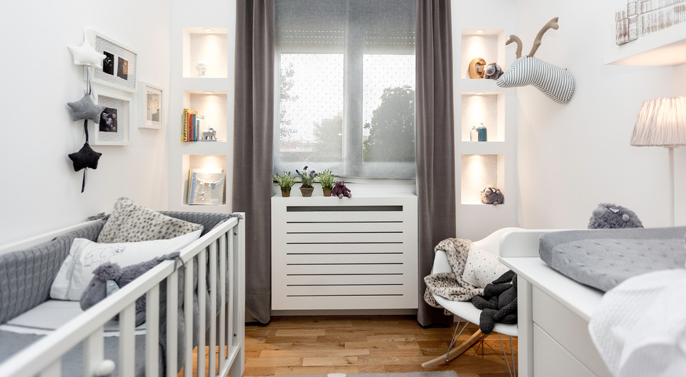 Idée de décoration pour une chambre de bébé neutre nordique de taille moyenne avec un mur blanc et un sol en bois brun.