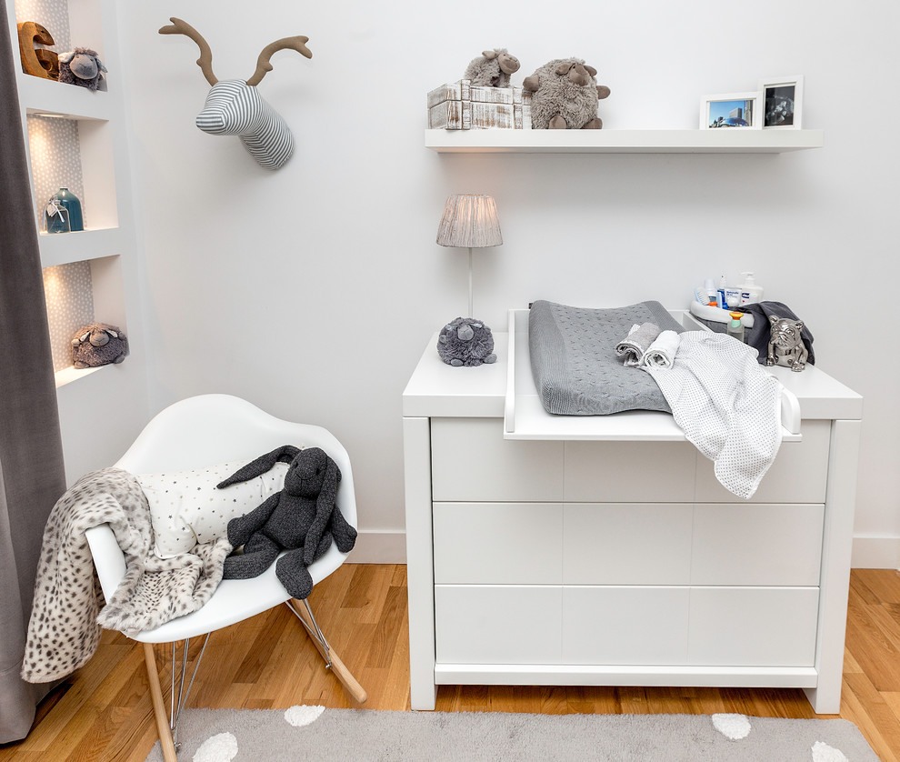 Diseño de habitación de bebé neutra escandinava de tamaño medio con paredes blancas y suelo de madera en tonos medios