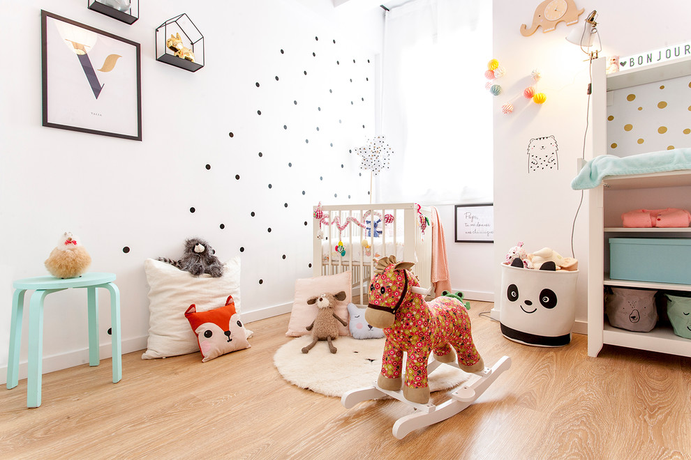 Foto di una piccola cameretta per neonata nordica con pareti bianche, pavimento marrone e pavimento in legno massello medio