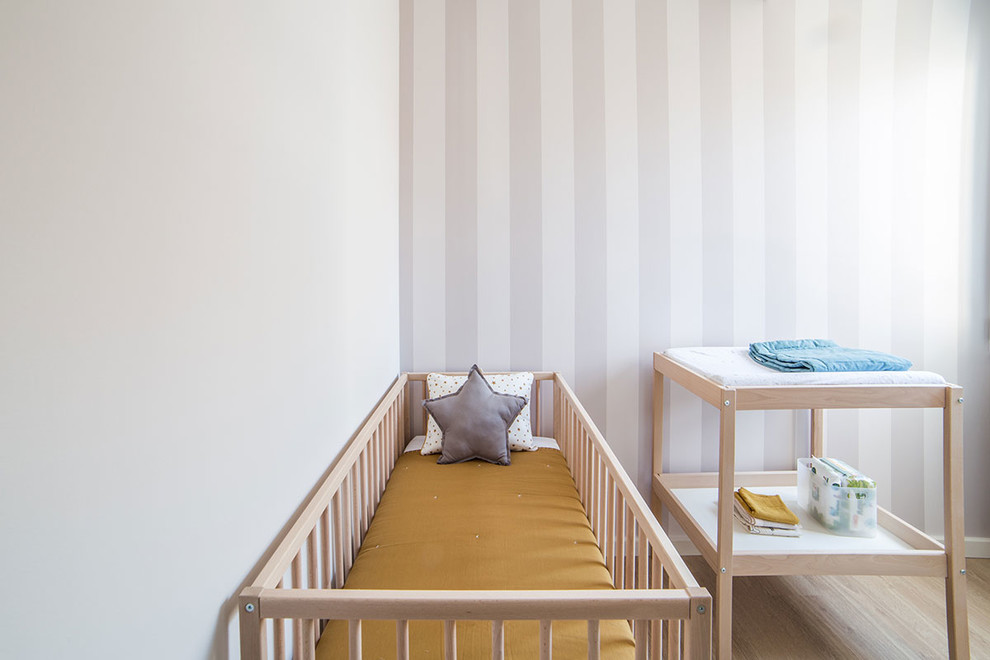 This is an example of a small scandi gender neutral nursery in Barcelona with white walls and light hardwood flooring.