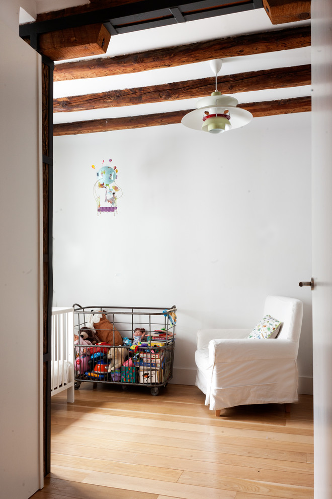Ejemplo de habitación de bebé neutra minimalista grande con paredes blancas y suelo de madera en tonos medios