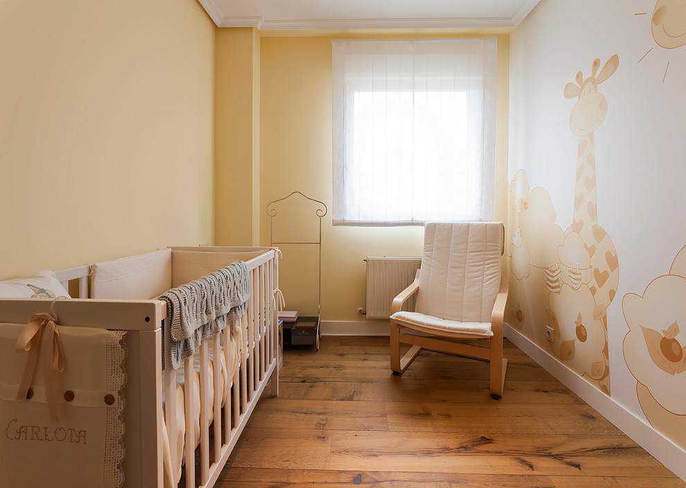 Réalisation d'une chambre de bébé neutre tradition de taille moyenne avec un mur jaune et un sol en bois brun.