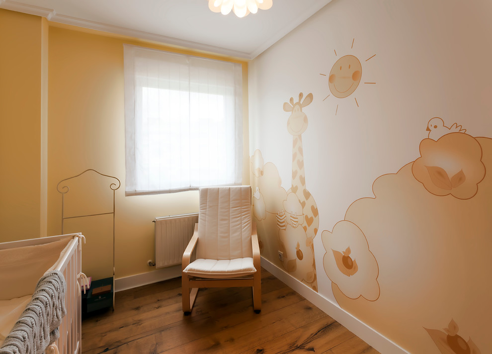 Ejemplo de habitación de bebé neutra tradicional renovada de tamaño medio con paredes amarillas y suelo de madera en tonos medios