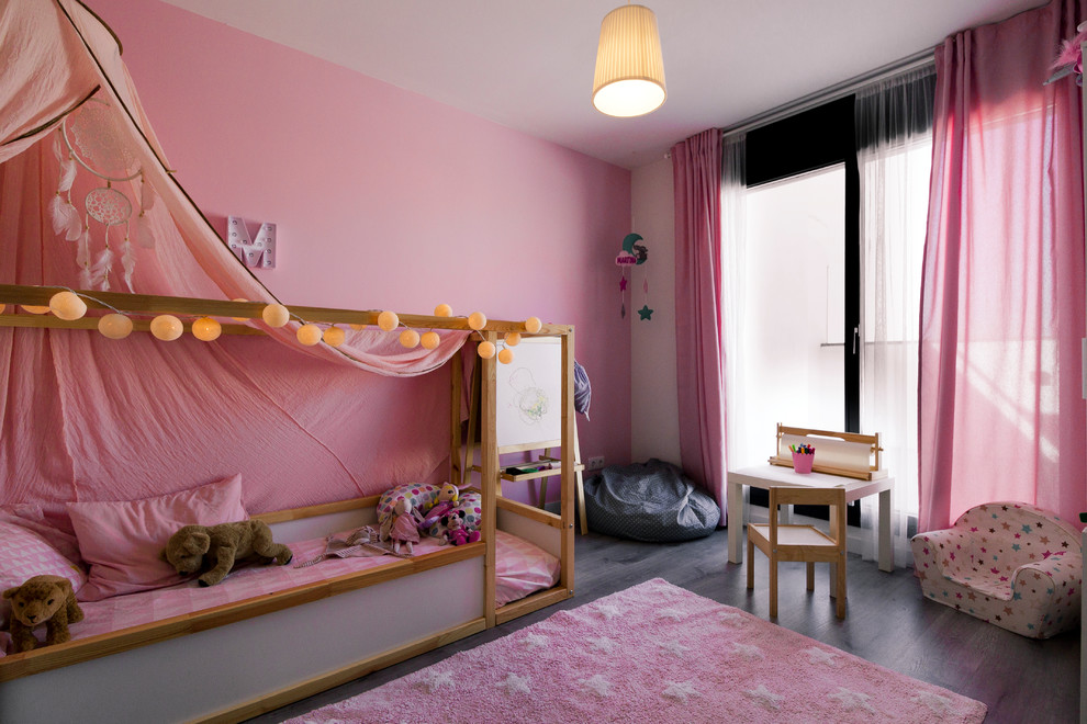 Imagen de habitación de bebé neutra actual pequeña con paredes rosas, suelo laminado y suelo marrón