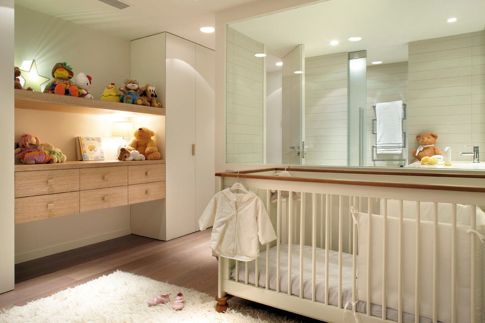 Diseño de habitación de bebé neutra contemporánea grande con paredes blancas, suelo de madera en tonos medios y suelo marrón