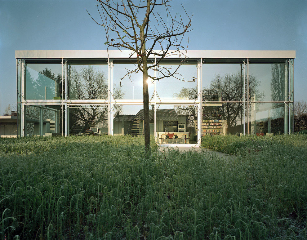 This is an example of a medium sized modern two floor glass house exterior in Stuttgart with a flat roof.