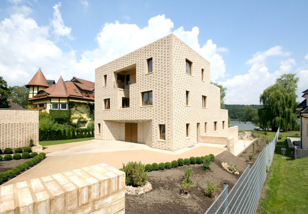 Diseño de fachada beige mediterránea grande de tres plantas con revestimiento de ladrillo y tejado plano