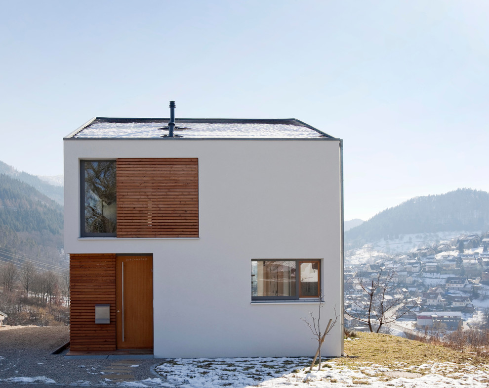 На фото: двухэтажный, белый, маленький дом в современном стиле с двускатной крышей и облицовкой из цементной штукатурки для на участке и в саду