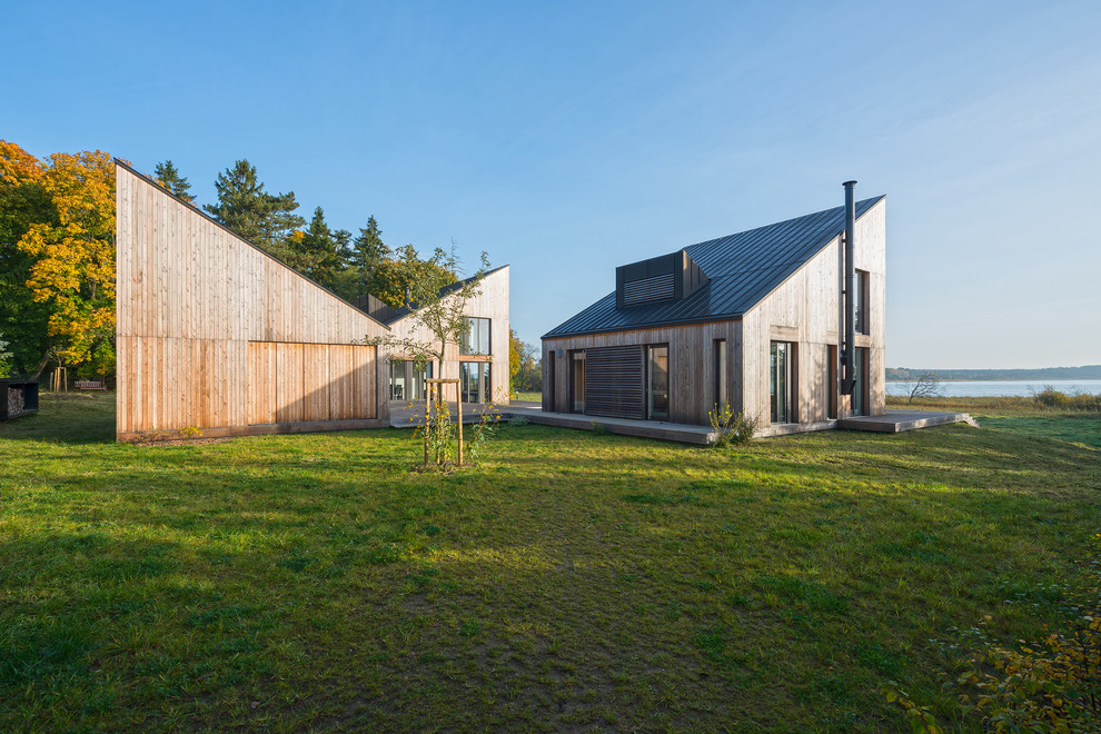 На фото: деревянный, бежевый, двухэтажный частный загородный дом среднего размера в современном стиле с односкатной крышей и металлической крышей